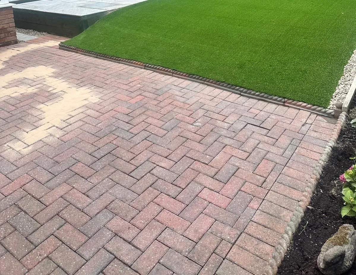 Herringbone block paving beside an artificial lawn