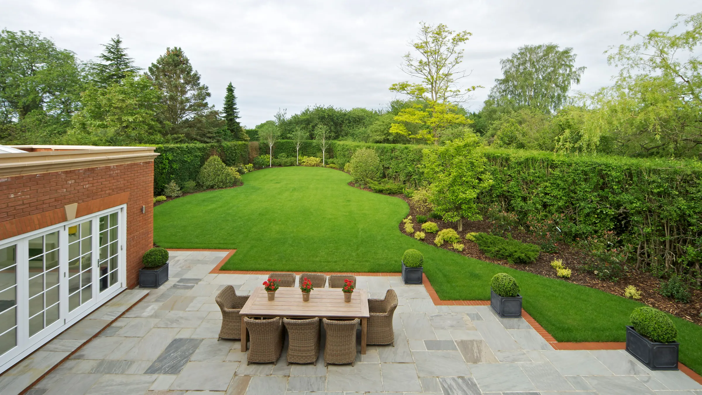 Rear garden with a sandstone patio, lawn and hedges