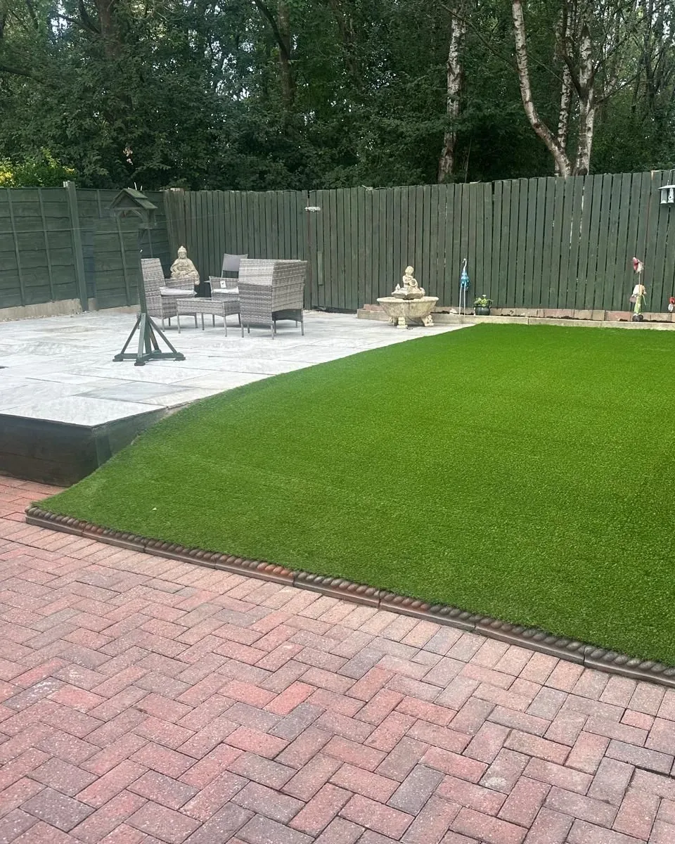 A new artificial lawn beside a sandstone patio and a red herringbone block paved path in a Manchester back garden