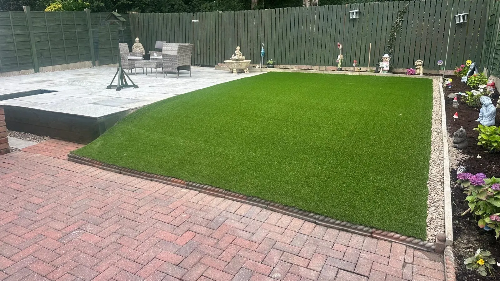 A new artificial lawn beside a sandstone patio and a red herringbone block paved path in a Manchester back garden