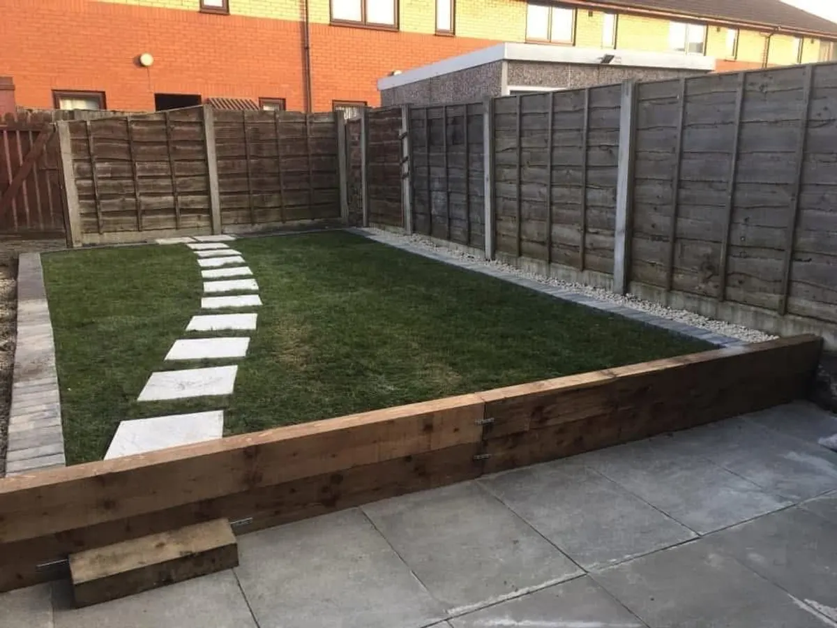 Sleeper retaining wall holding a raised turf lawn above a patio in Manchester