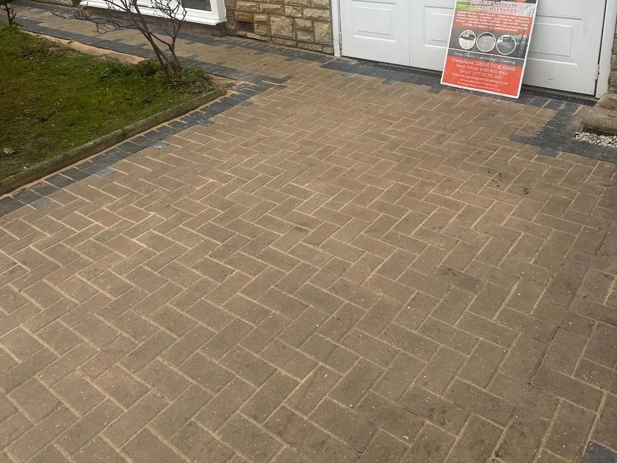 Buff herringbone block paving with a charcoal border laid up to a garage in Manchester