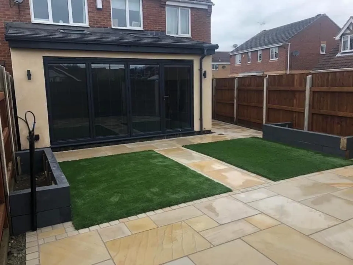 Rear garden landscaped with a sandstone patio, artificial grass and raised beds in Manchester