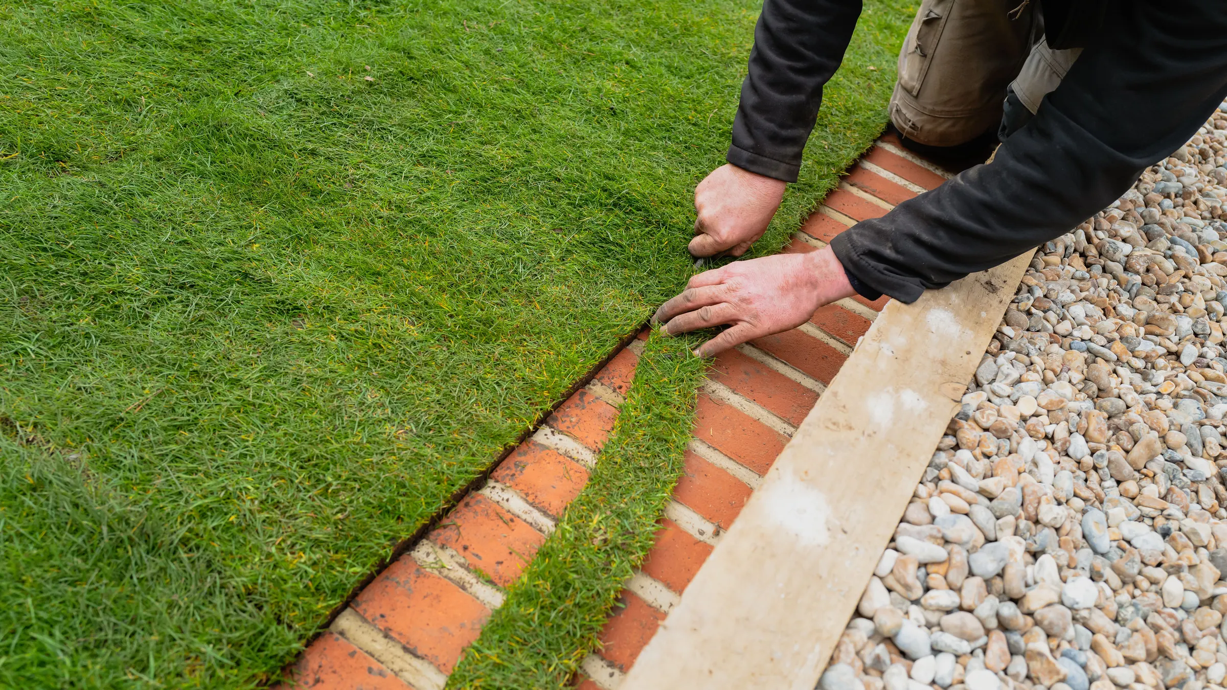 New turf being laid against a brick edge